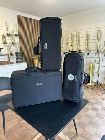 GEWA Triple Symphony trumpet cases displayed in a music store with various brass instruments in the background.